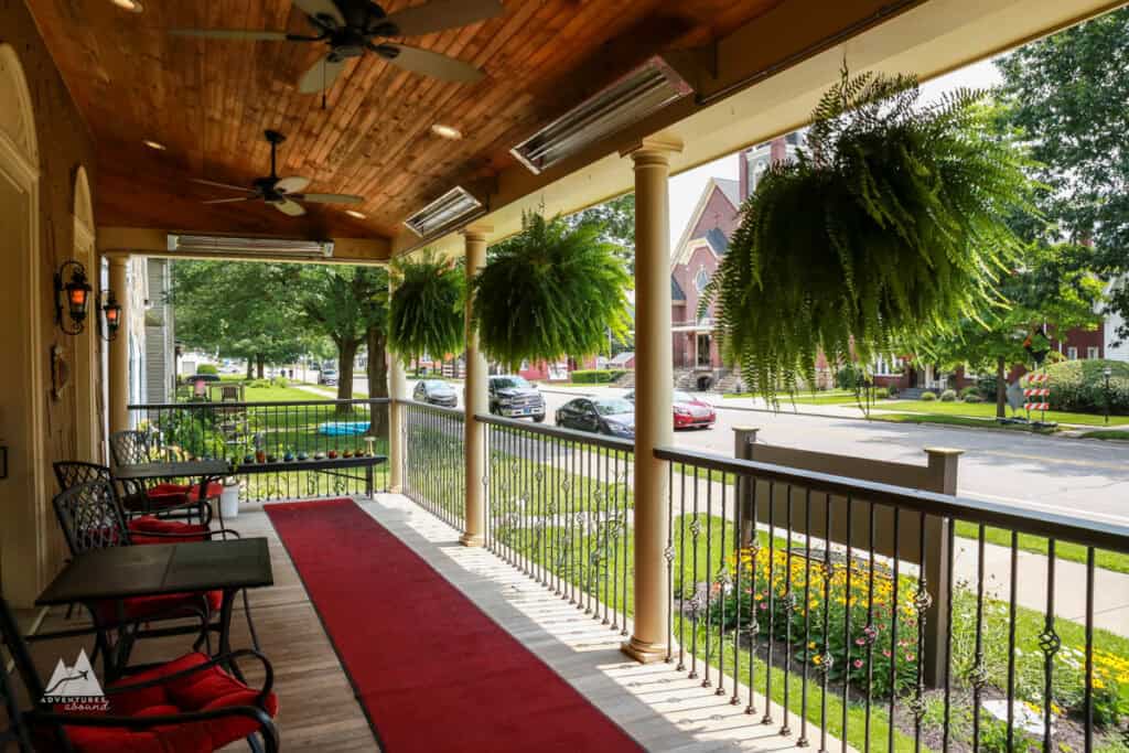 A view from the front porch of Hygrade Inn, with a red runner rug in front of seating, ceiling fans, and large green ferns hanging from the edge.