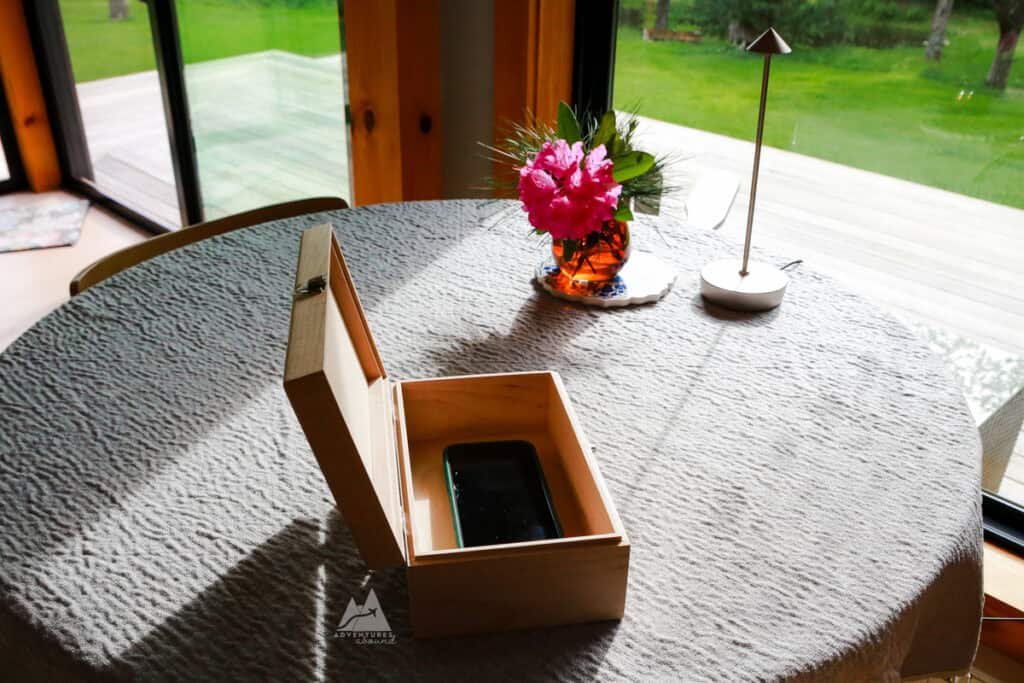 A phone sits with its screen off inside of a light wooden box with the lid open, a sign of unplugging at the cabin.
